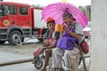 Lady, Blind Man beside disabled Beggar in wheelchair at Church yard Gate Portal with umbrella