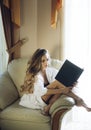 Lady with busy face in bathrobe reads book near window.