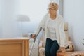 Lady with a cane gets up from a chair from a room in a retirement home