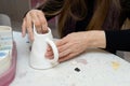 lady cleans white pitcher with sandpaper before applying pattern to clay milk jug in workshop