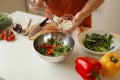 Woman putting cut feta cheese into bowl with tasty salad on table in kitchen and light blur background. Royalty Free Stock Photo