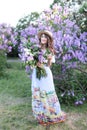 A lady in an elegant long dress, in a straw hat and a neat hairdo is standing in a summer garden. A young girl in a hat holds lila Royalty Free Stock Photo