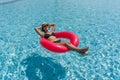 A lady enjoy a sunny day, floating on a bright inflatable ring in a clear blue swimming pool Royalty Free Stock Photo