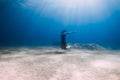 Lady freediver with fins posing and glides underwater in blue sea with sunlight Royalty Free Stock Photo