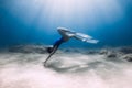 Lady freediver with fins posing and glides underwater in blue sea with sunlight Royalty Free Stock Photo