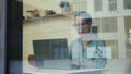 A lady in glasses working with a computer seen through the window