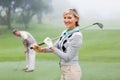 Lady golfer smiling at camera with partner behind Royalty Free Stock Photo