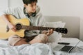 Lady in headphones is reading chords from the screen of laptop and playing on acoustic guitar