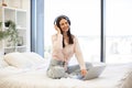 Lady in headphones sitting on bed and enjoying online chatting on weekend. Royalty Free Stock Photo