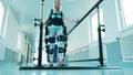 A lady is learning to walk in the exosuit with medical help