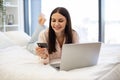 Lady lying on bed and enjoying purchase of goods on Internet using bank card.