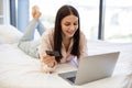 Lady lying on bed and enjoying purchase of goods on Internet using bank card.