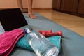 Lady making muscular flooring class at home with her iPad in yoga mat and towel. Bottle of water and pink dumbbells on a mattress