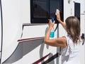 A lady motorhome owner cleans her windows.She has a spray gun with blue cleaning liquid in one hand and cleans the window cloth Royalty Free Stock Photo