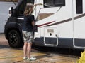 Lady motorhome owner stands in shorts cleaning her recreational vehicle with a hose pipe.Spray can be seen on sunny day Royalty Free Stock Photo