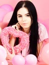 Lady in pajamas with symbol of love, pink heart. Girl lay near balloons, holds heart toy, pink background. Brunette on