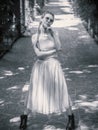 A lady with pigtails in a tutu and rough shoes stands in a pose with her hand supporting her chin on an alley in a Royalty Free Stock Photo