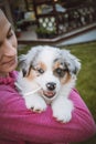 Lady in a pink sweatshirt holding a smiling Australian Shepherd puppy. Love and relationship between female dog and female. Magic