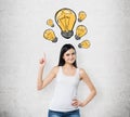 Lady is pointing out the drawn yellow light bulbs. A concept of new ideas and creativity. Concrete background. Royalty Free Stock Photo