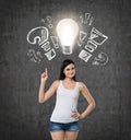 Lady is pointing out the light bulb and drawn question, exclamation marks. Dark concrete background. Royalty Free Stock Photo