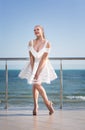 A lady posing on a hotel`s terrace. The smiling female on a bright sky background. The stylish girl in a short white dress. Royalty Free Stock Photo