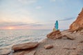 Lady on rock with surfboard and suitcase. Sunset over horizon, sea view. Surfing time, summer vacation idea. Copy space Royalty Free Stock Photo