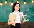 Lady scientist holds book and microscope, chalkboard on background, copy space. Lady in formal wear on calm face in