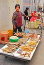 An elderly Asian lady selling various types of dried fish