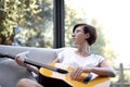 Lady with short black hair and glasses playing the guitar on the couch Royalty Free Stock Photo