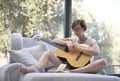 Lady with short black hair and glasses playing the guitar on the couch Royalty Free Stock Photo