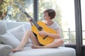 Lady with short black hair and glasses playing the guitar on the couch Royalty Free Stock Photo