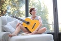 Lady with short black hair and glasses playing the guitar on the couch Royalty Free Stock Photo