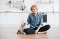 Lady sitting cross-legged in kitchen with small dog