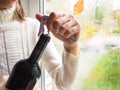 Lady sitting on the windowsill opens a bottle of wine with a corkscrew. Royalty Free Stock Photo