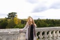 Lady standing near concrete railing with tree background.