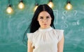 Lady strict teacher on calm face stands in front of chalkboard. Woman with long hair in white blouse stands in classroom Royalty Free Stock Photo