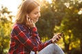 Lady student sitting in the park using mobile phone listening music. Royalty Free Stock Photo