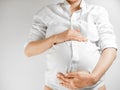 Lady in the third trimester of pregnancy. A pregnant young woman in white shirt grabbed her belly white background. A