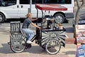 A lady on a three wheeled bike selling drinks .