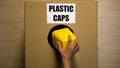 Lady throwing plastic caps in cardboard box collecting reusable material utilize