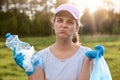 Lady with twisted face wearing blue latex gloves, holding rubbish in hands, looks at camera with upset facial expression, wants to