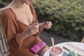 A lady twists open her dark shade of red liquid glossy finish lip tint while her wallet is placed on her lap