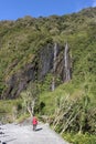 Lady walking on valley footpath, waterfall at side