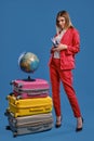 Lady in white blouse, red pantsuit, black heels. Smiling, holding passport and ticket, posing on blue background. Globe Royalty Free Stock Photo