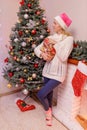 Lady in white sweater and Santa hat stand with gift box near fireplace and dreaming, Royalty Free Stock Photo