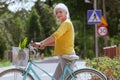 Lady in a yellow blouse crosses the street leading a blue bicycle