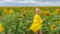 Joyful adult in a yellow dress with a beautiful smile on the background of sunflowers with blue clouds on a summer day