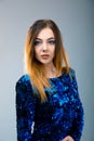 Ladylike redhead woman in the blue evening sparkling dress is posing over grey background