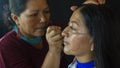 Woman of the Quichua ethnic group of the Ecuadorian Amazon applying makeup to her sister`s face in traditional dress on a black