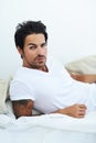 Laid-back cool. Portrait of ruggedly handsome man wearing a white t-shirt and lying on a bed. Royalty Free Stock Photo